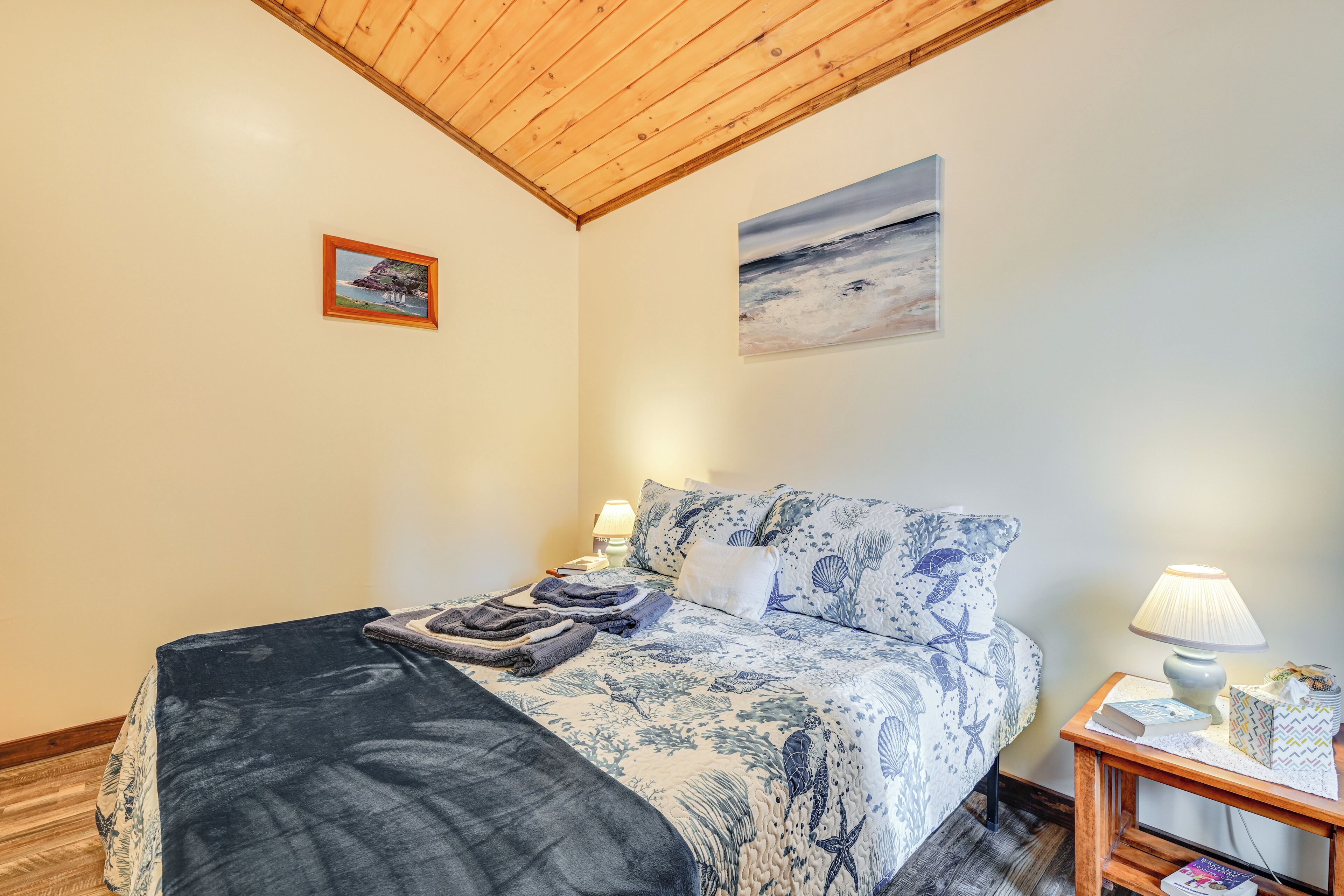A bedroom with a bed, a nightstand, a lamp, and two wall-mounted pictures.