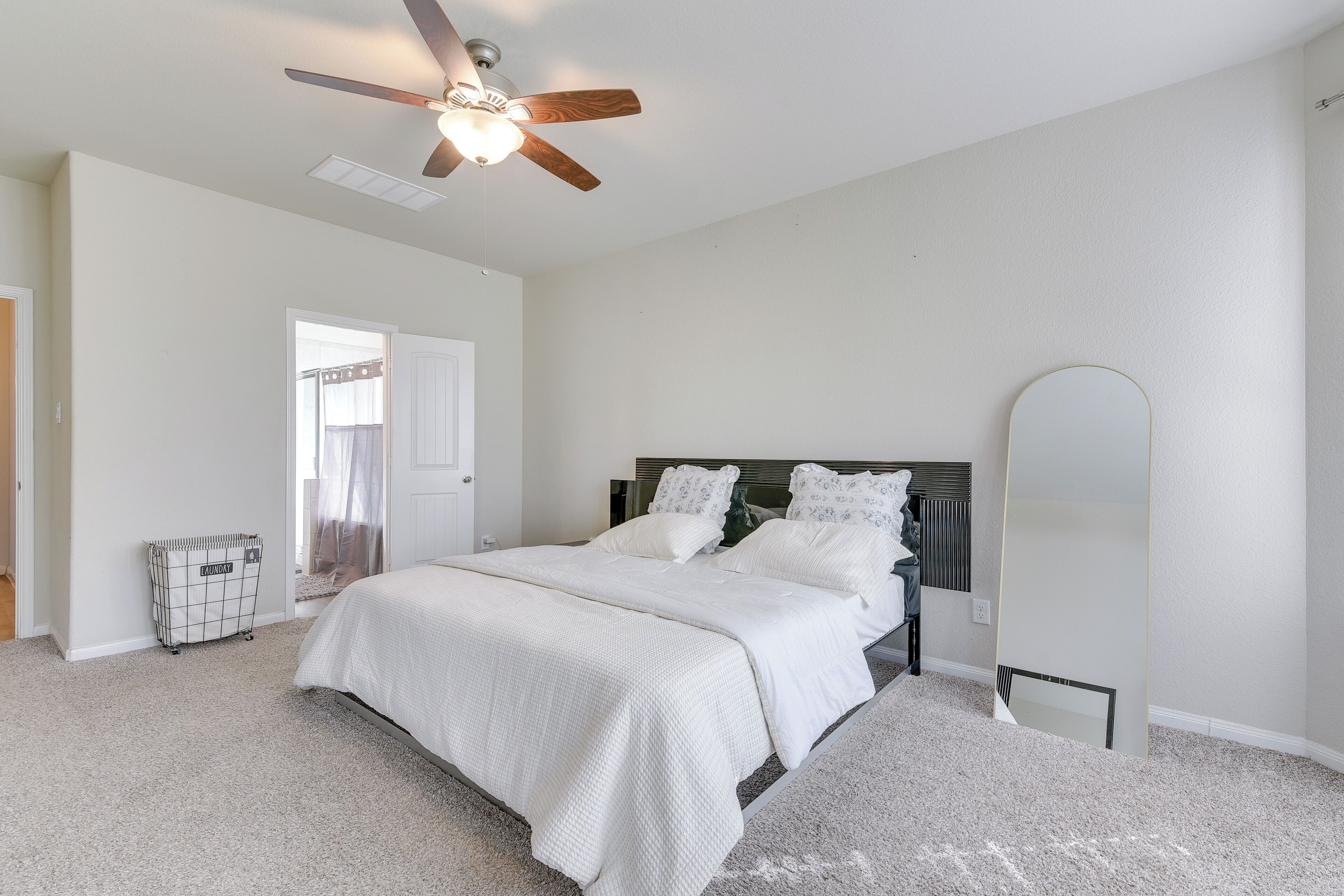 A bedroom with a bed, a ceiling fan, a large mirror, and a laundry cart.