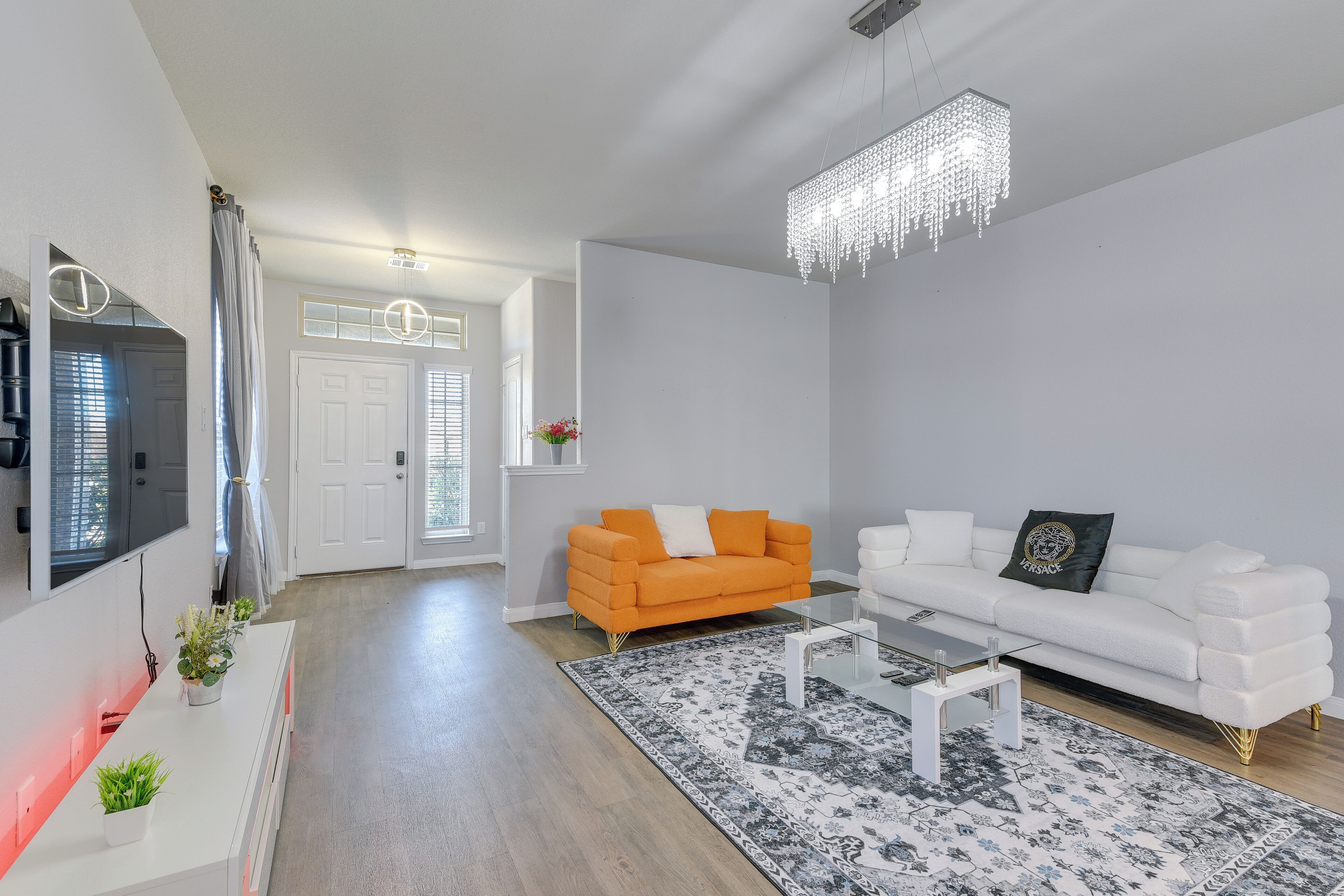 A modern living room with a white sofa, an orange sofa, a glass coffee table, and a patterned rug.