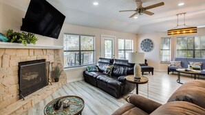 A living room with a stone fireplace, leather sofa, and a flat-screen TV mounted on the wall. - 300 Feet to Lake Texoma: Modern Home w/ Deck! (Kingston)