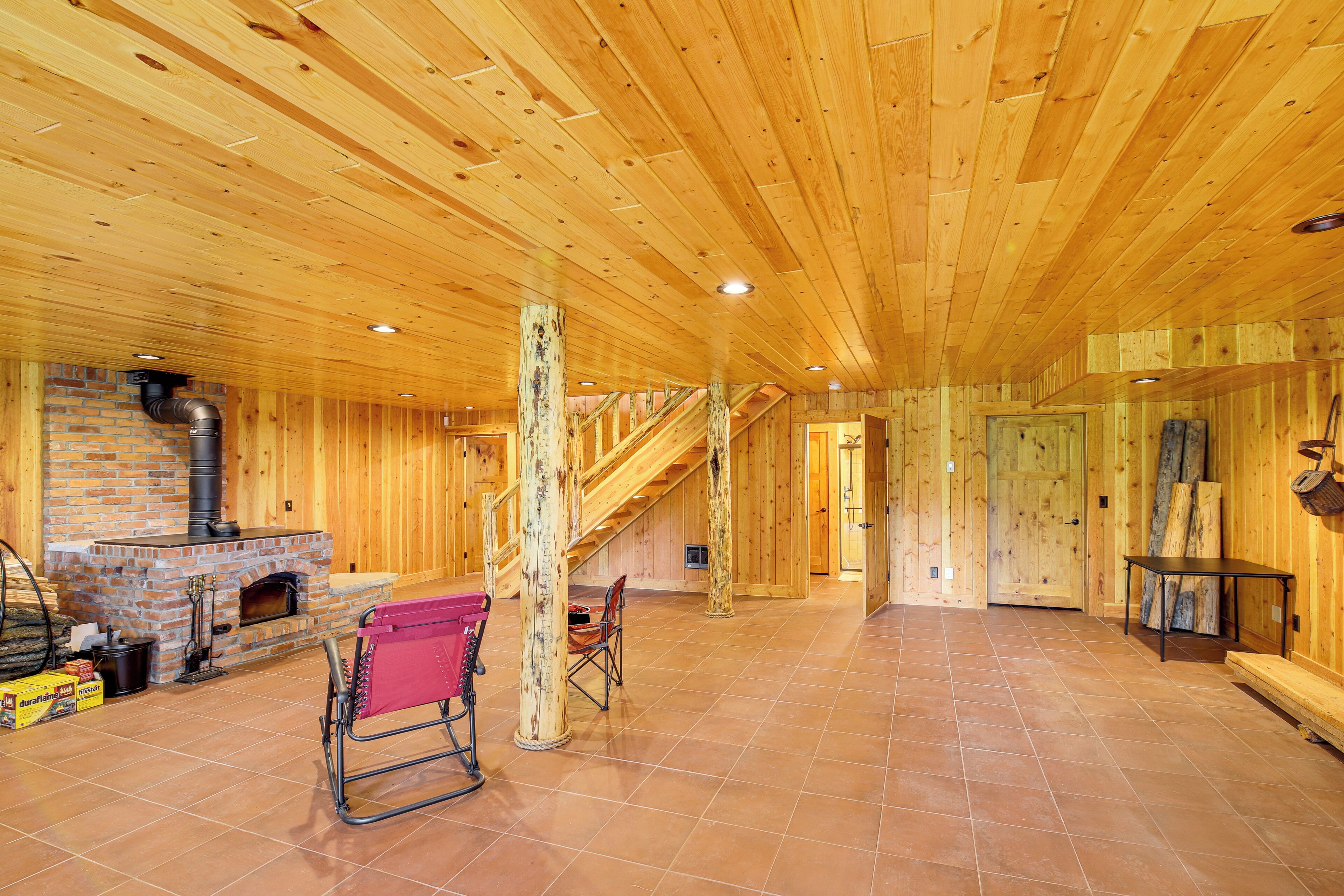 Ein geräumiges Zimmer mit Holzwänden und -decke, einem Kamin aus Backstein und einer Treppe, die zu einer anderen Ebene führt.