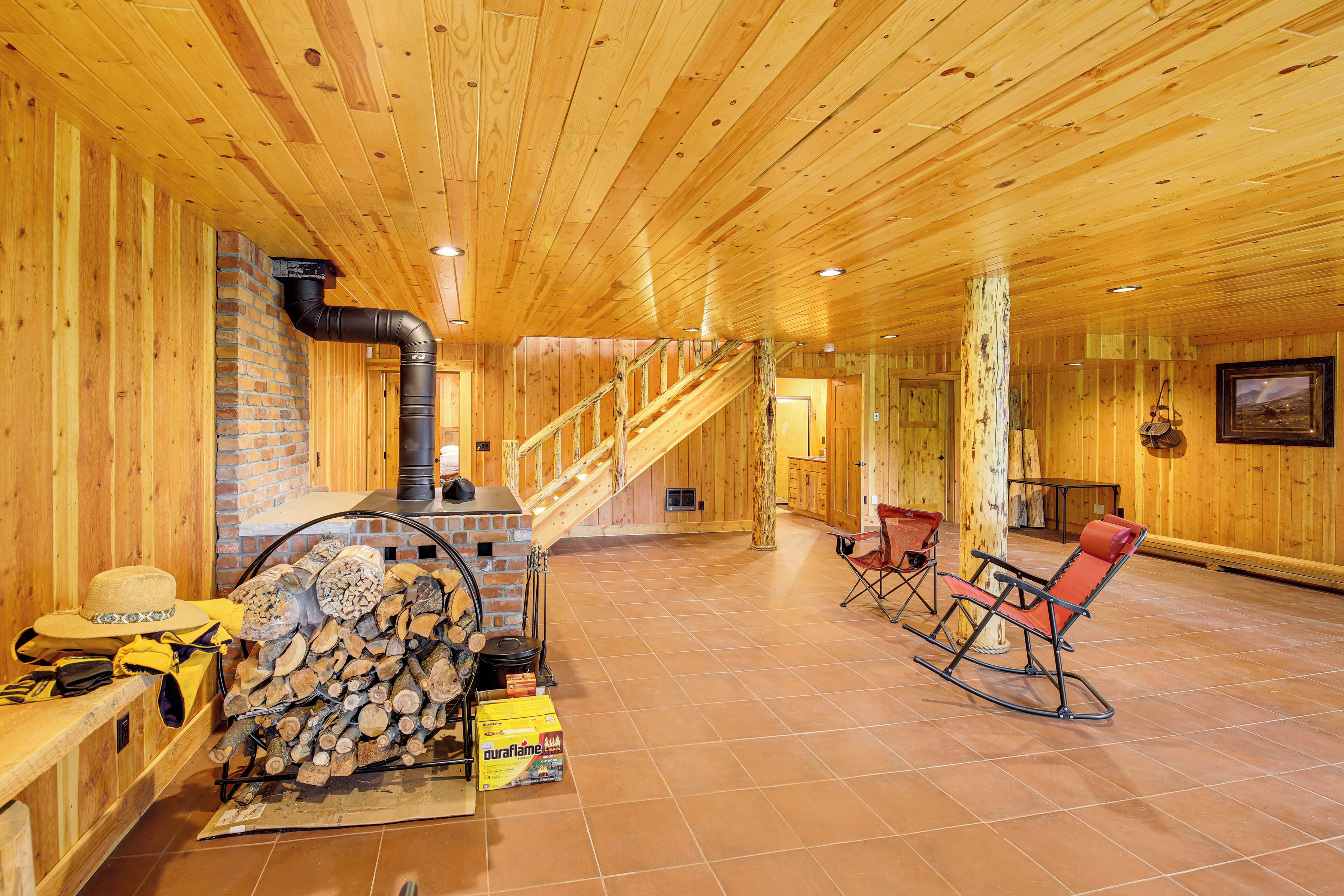 A wooden interior with a fireplace, stacked firewood, and a dining area with chairs.