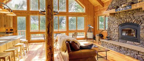 A spacious cabin with large windows, a stone fireplace, and a leather sofa.
