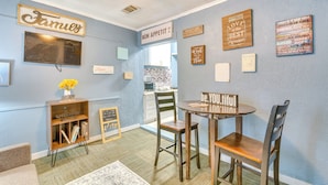 A cozy room with a blue wall, a wooden cabinet with 'welcome' and 'home' signs, a round table with two chairs, and various inspirational wall art.