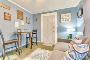 A living room with a blue wall, a wooden dining table with chairs, a sofa with striped pillows, and a door with a white frame. - Centrally Located North Little Rock Studio w/ Yard (North Little Rock)