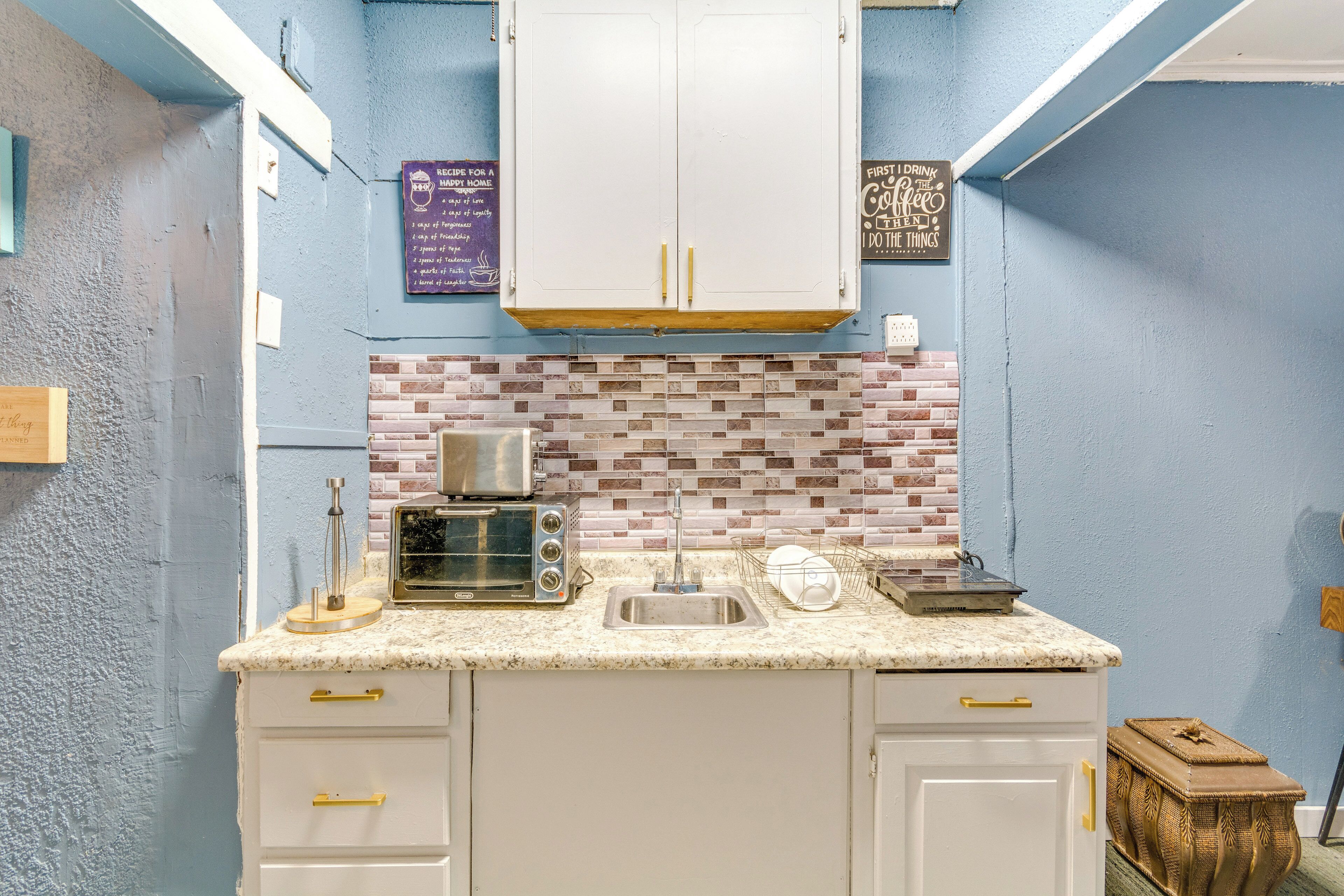 A kitchen with white cabinets, a brick backsplash, a toaster, and a sink.
