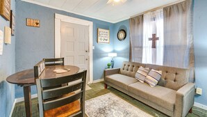 A living room with a blue wall, a beige sofa, a wooden dining table with chairs, a ceiling fan, and a clock on the wall.