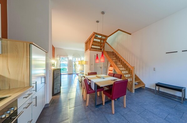 A modern kitchen with wooden cabinets, a dining area with a wooden table and red chairs, and a staircase leading to an upper level. - Vacation apartment "Schwan" with large terrace in Jabel an der Müritz (Jabel)