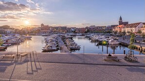 En lysthavn med fortøjede både, en brostensbelagt sti og bygninger i baggrunden.