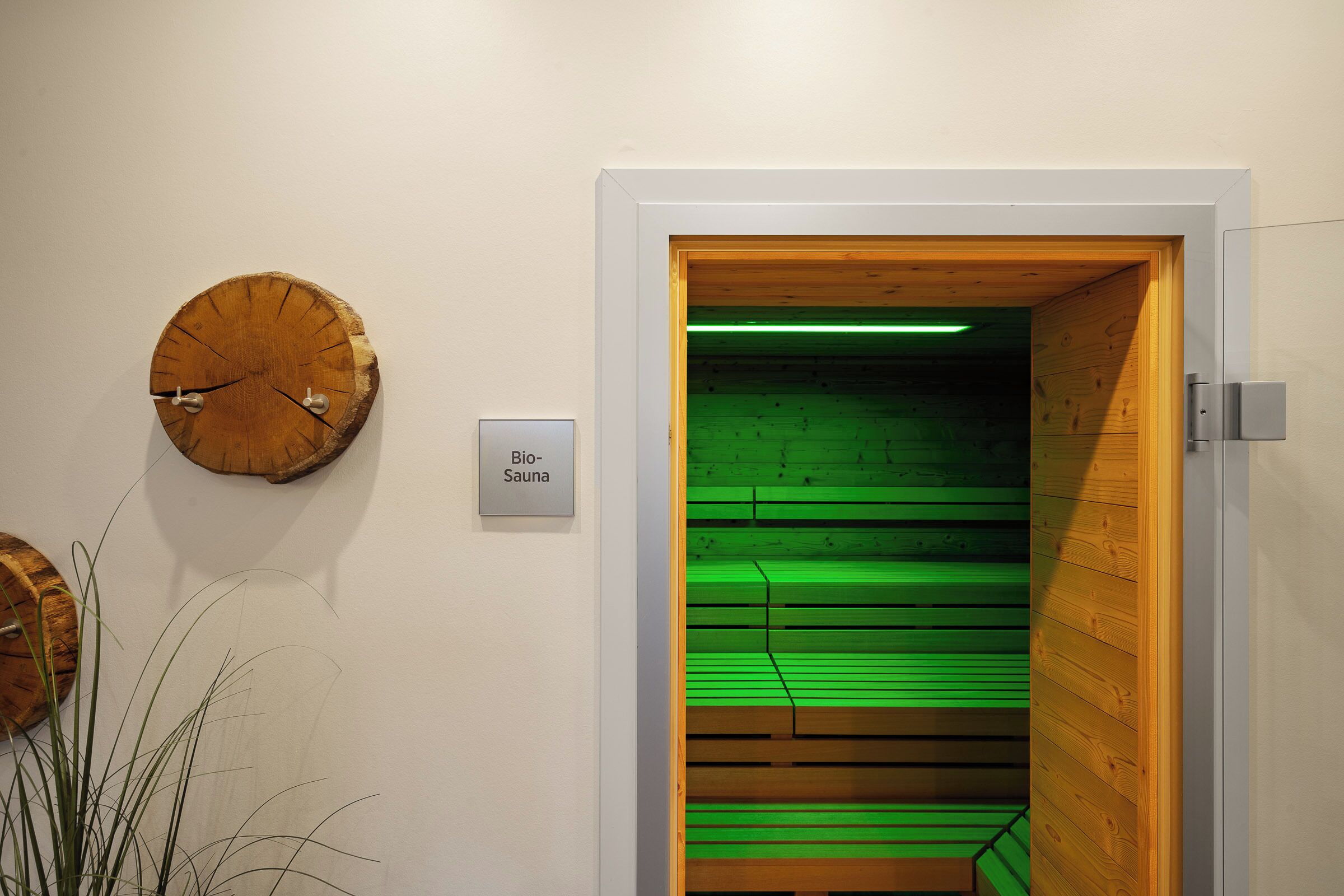 A room with a wooden door leading to a sauna area, a wall-mounted clock, and a sign indicating the sauna location.