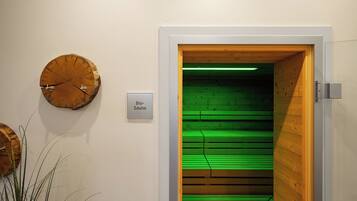 A room with a wooden door leading to a sauna area, a wall-mounted clock, and a sign indicating the sauna location.