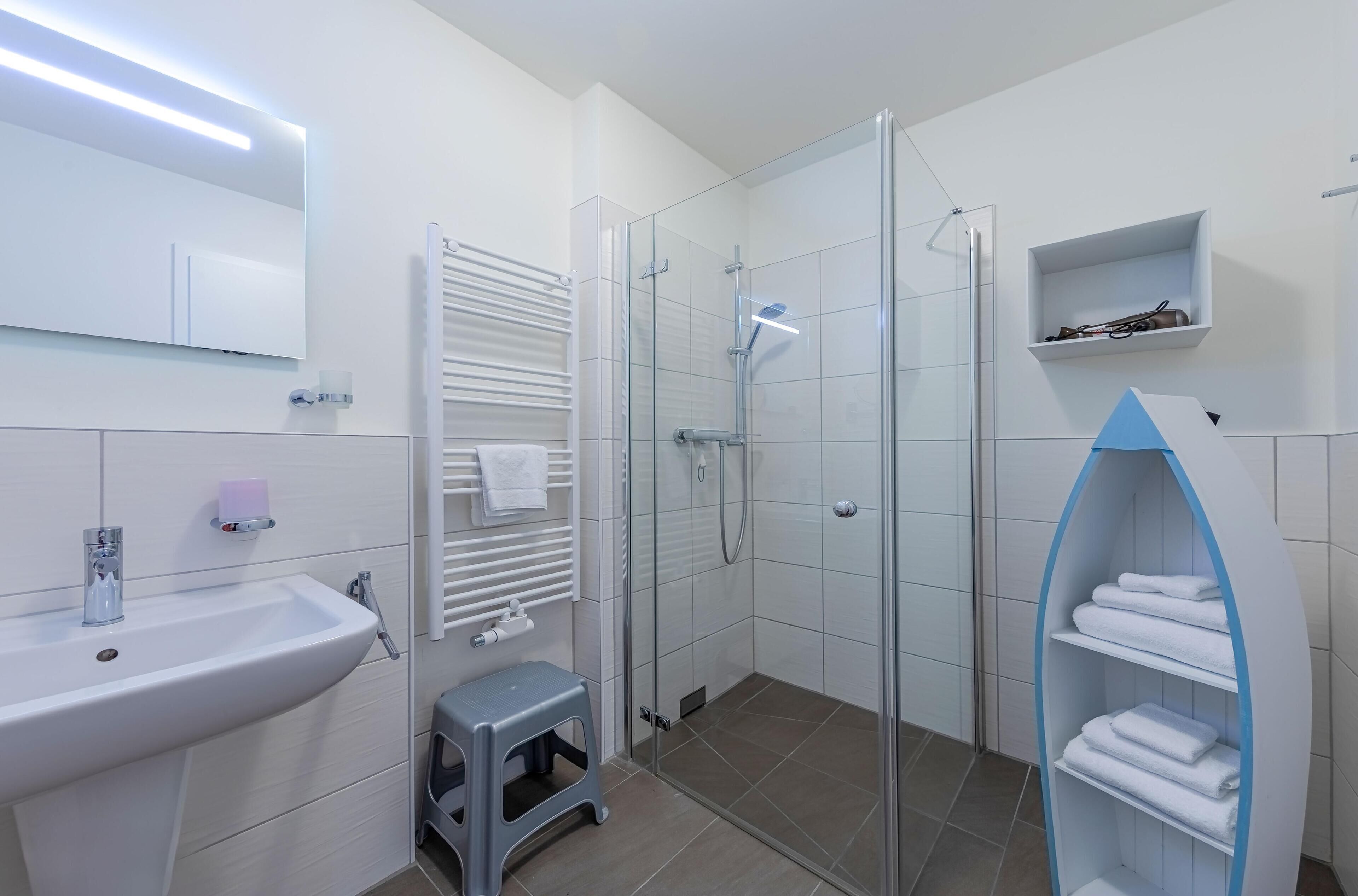 A modern bathroom with a glass-enclosed shower, a white sink, and a towel rack.