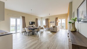 Una habitación de hotel moderna con comedor, sofá, televisión y un ventanal grande.