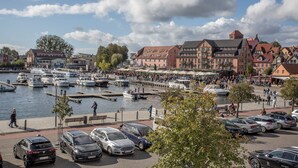 Una zona ribereña con barcos amarrados, un paseo peatonal y coches aparcados.