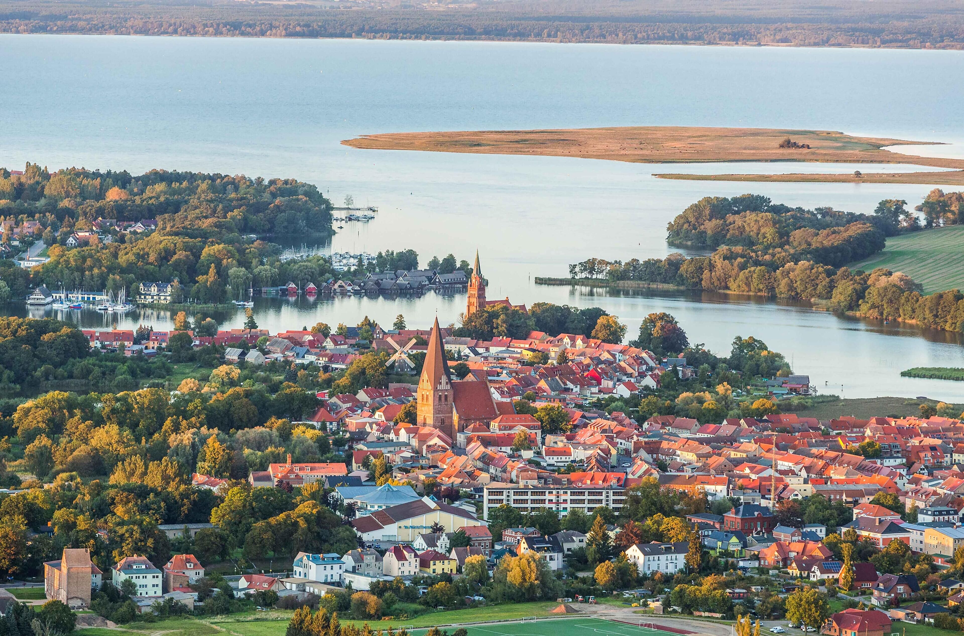 A town with a prominent church and windmill, surrounded by water and greenery.