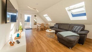 Un salon moderne avec un canapé, une table basse et un téléviseur fixé au mur. On peut voir des fenêtres de toit et un balcon.