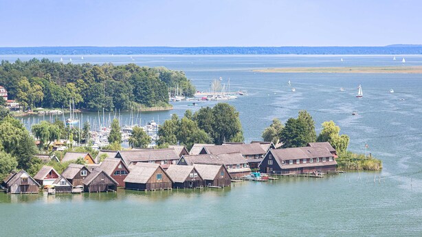 Une propriété située au bord de l’eau, comprenant plusieurs bâtiments en bois, un quai et des bateaux en arrière-plan.