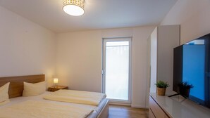 Une chambre moderne avec deux lits, une télévision et une fenêtre équipée de stores.