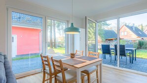 Un espace repas moderne avec une table et des chaises en bois, de grandes fenêtres et une vue sur un bâtiment rouge et la verdure environnante.