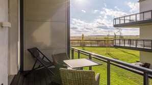 Ein Balkon mit Korbstühlen und einem Tisch, der auf eine Wiese und eine entfernte Landschaft blickt.