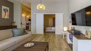 Ein modernes Wohnzimmer mit einer Couch, einem Couchtisch und einem Fernseher. Es gibt eine Küchenzeile mit einer Mikrowelle und einem Esstisch.