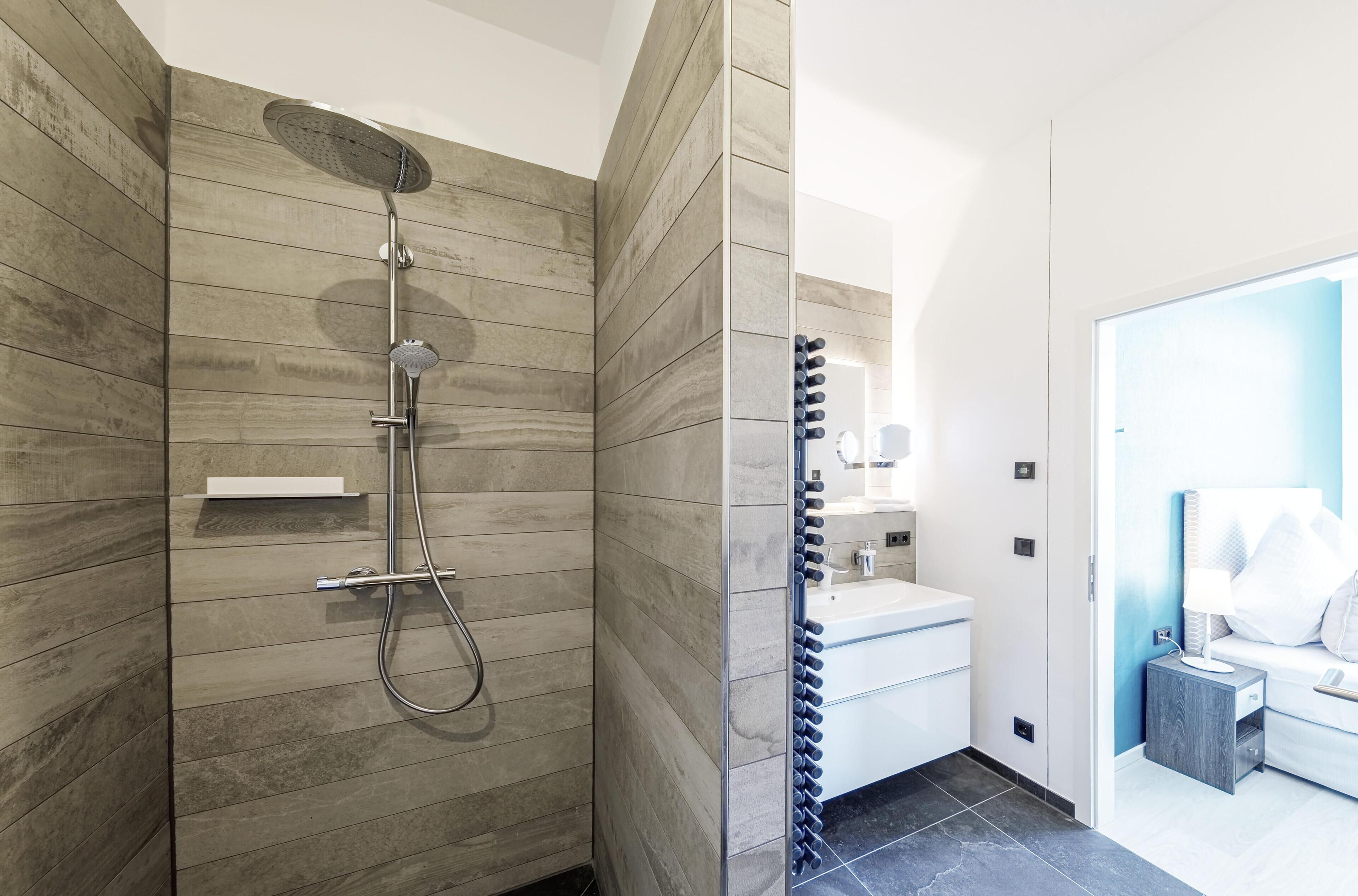 A modern bathroom with a shower, vanity, and a bed in the adjacent room.