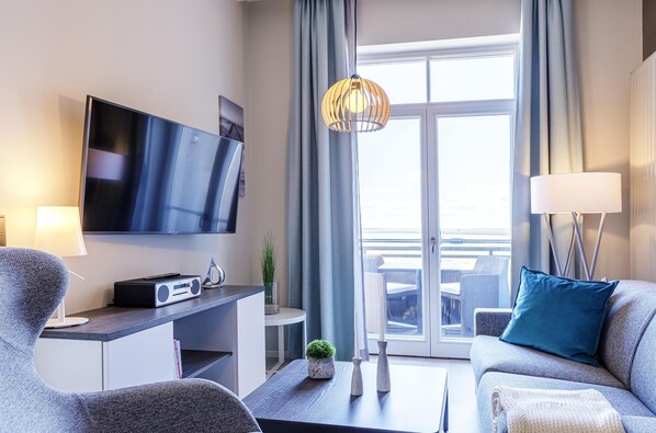 En moderne stue med et fladskærms-tv, en sofa, et sofabord og udsigt til en balkon.
