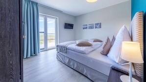 A modern bedroom with a bed, a TV, and a view of the outdoors. - 5-star vacation apartment Boddenkieker between the Baltic Sea and the Bodden (Wustrow)