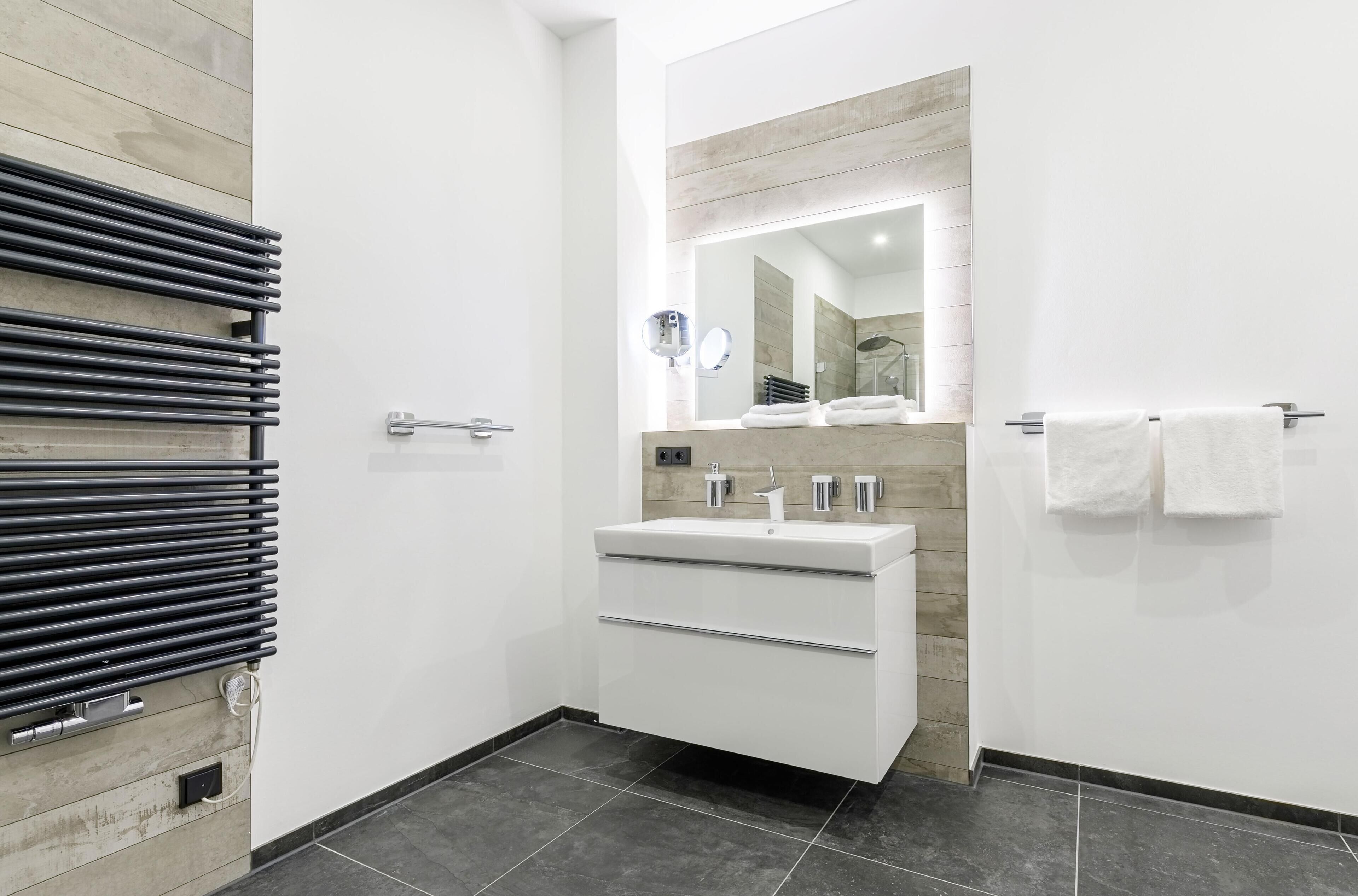 A modern bathroom with a white vanity, a mirror, and a towel rack.