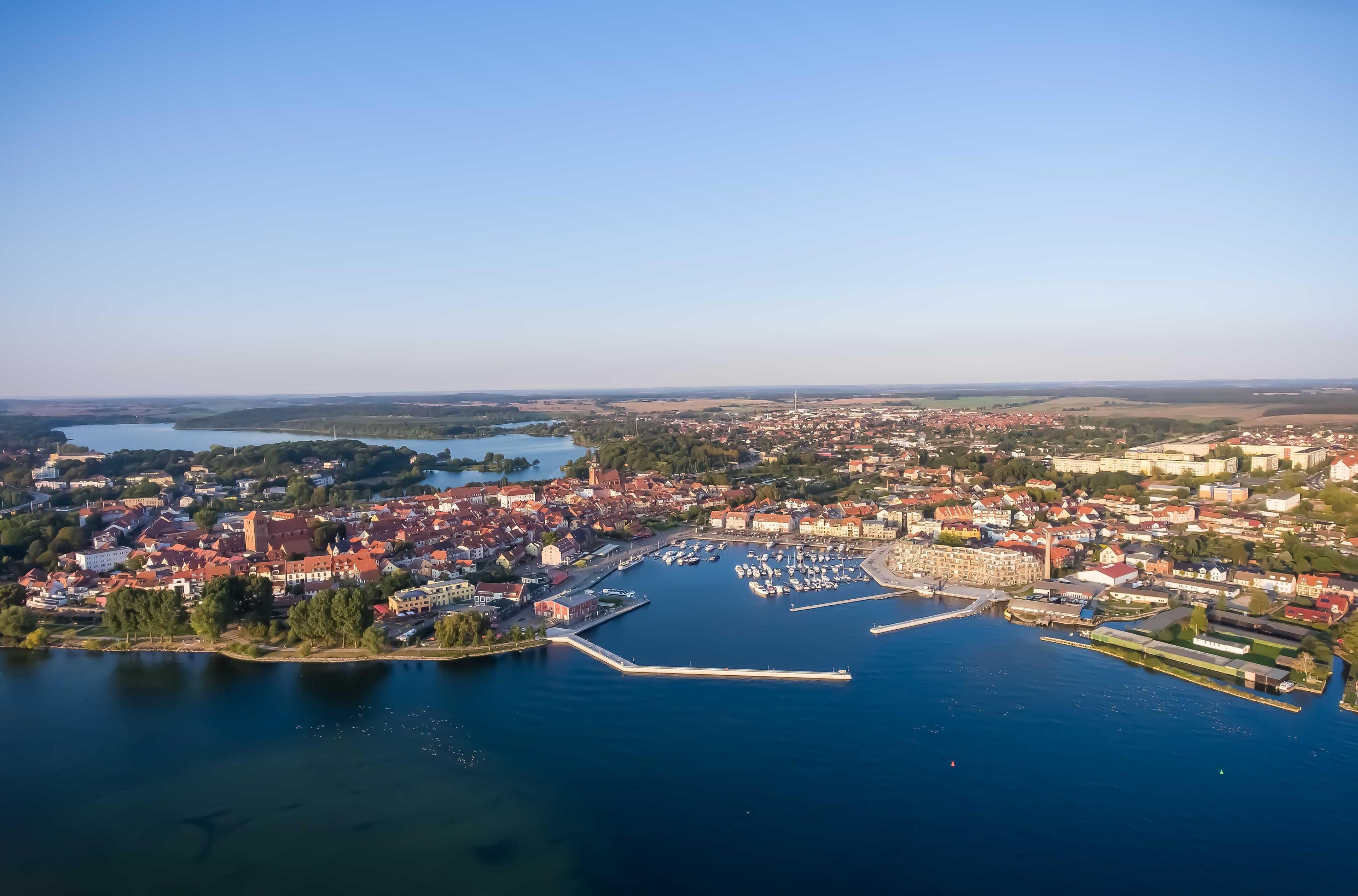 Vista aèria d'una població costanera amb un port esportiu, edificis i una extensa superfície d'aigua.