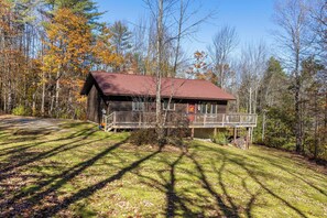 Une cabane dotée d’une terrasse, entourée d’arbres et bordée d’une zone herbeuse.