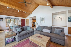 Una sala de estar acogedora con techo de madera, un sofá modular gris, una mesa de centro de madera y una puerta roja.