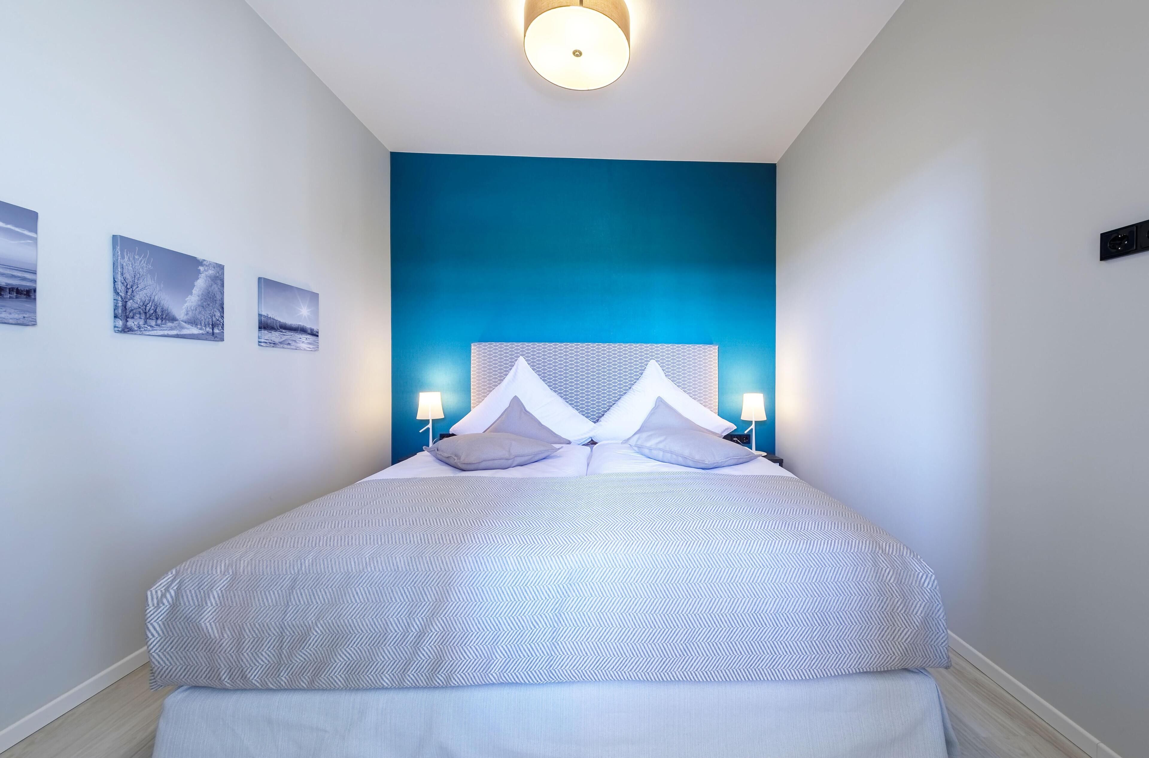 Ein modernes Schlafzimmer mit einem großen Bett, zwei Nachttischlampen und drei gerahmten Bildern an der Wand.