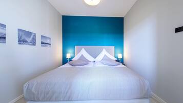 Ein modernes Schlafzimmer mit einem großen Bett, zwei Nachttischlampen und drei gerahmten Bildern an der Wand.