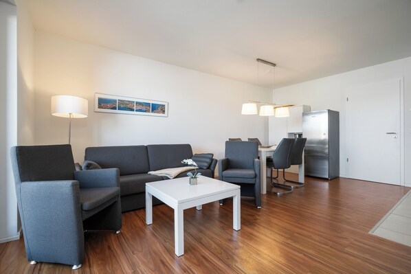Un salon moderne avec un canapé gris, deux fauteuils, une table basse blanche et un coin repas comprenant une table et des chaises.