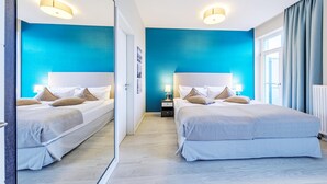 A modern hotel room with two beds, a large mirror, and a view of the city.