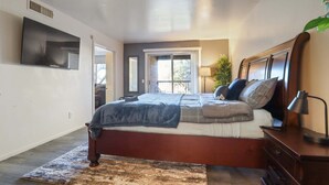 A bedroom with a bed, a TV mounted on the wall, a window, and a plant. - Hoff Gardens 38 - 1BR/1BA - Downtown Lubbock (Lubbock)