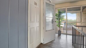 A hallway with a white door marked '38', a potted plant, and a balcony with a railing. - Hoff Gardens 38 - 1BR/1BA - Downtown Lubbock (Lubbock)