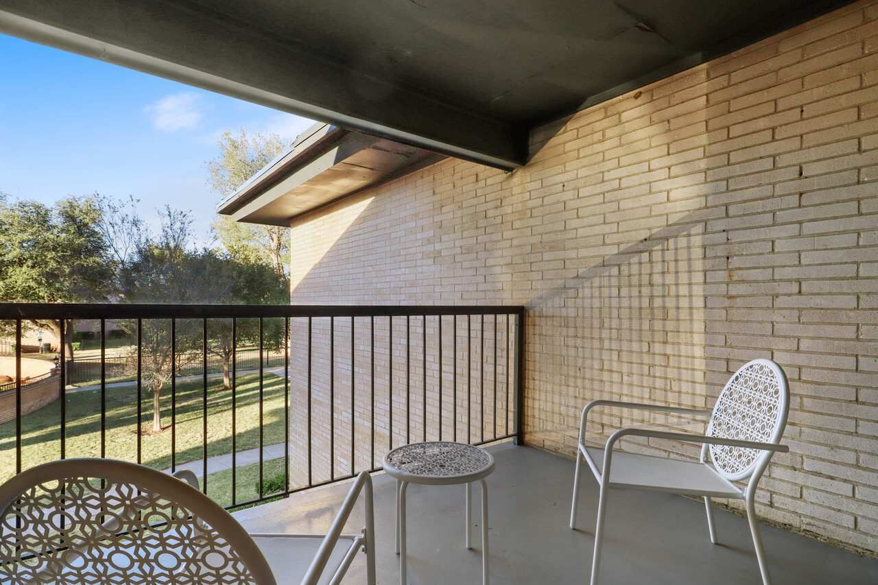 A balcony with a brick wall, a metal railing, and two white chairs.