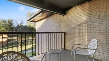 A balcony with a brick wall, a metal railing, and two white chairs.