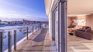 En balkong med utsikt över en småbåtshamn och stadens silhuett, en soffa och en lampa.