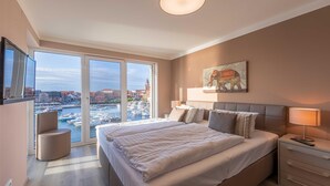 Ett modernt hotellrum med en stor säng, ett skrivbord och utsikt över en småbåtshamn.