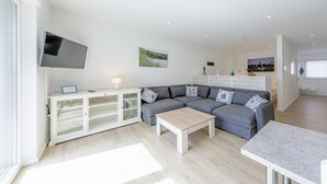 A modern living room with a grey sofa, a white cabinet, a flat-screen TV, and a wooden coffee table. - "Nordlicht" Vacation Rental in the Island Town of Malchow (Malchow)