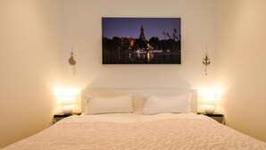 A neatly made bed with white linens, two bedside lamps, and a framed picture of a cityscape at dusk. - "Nordlicht" Vacation Rental in the Island Town of Malchow (Malchow)
