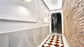 Um corredor com chão xadrez, paredes brancas e uma parede de tijolos em um dos lados.