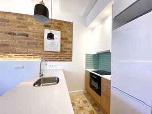 A modern kitchen with a brick wall, a stainless steel sink, a black pendant light, and a white refrigerator.