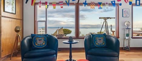 Une pièce avec deux fauteuils bleus, une petite table ronde et une vue sur la mer grâce à de grandes fenêtres.