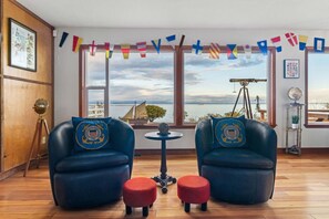 A room with two blue armchairs, a small round table, and a view of the sea through large windows. - Water Edge Coast-Guard Cottage-Panorama View- (Port Angeles)