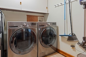 A laundry area with two front-loading washing machines and a blue broom leaning against the wall. - Water Edge Coast-Guard Cottage-Panorama View- (Port Angeles)