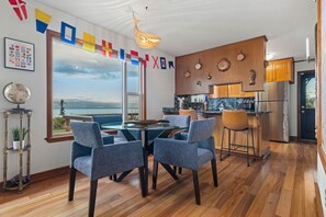 A modern kitchen with wooden cabinets, a stainless steel refrigerator, and a large window overlooking a scenic view. - Water Edge Coast-Guard Cottage-Panorama View- (Port Angeles)